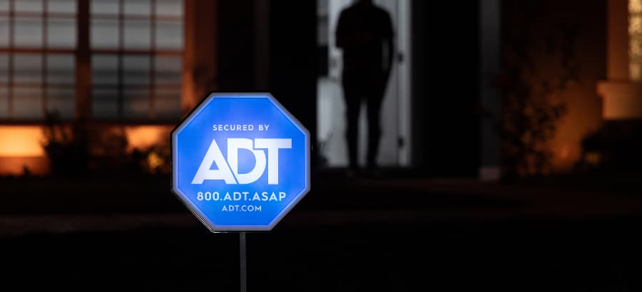 Blue ADT home security sign in yard of a home after dark.